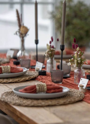 Gedeckter Tisch mit rustikalen Tellern, Kerzen, Servietten und dekorativen Blumen.