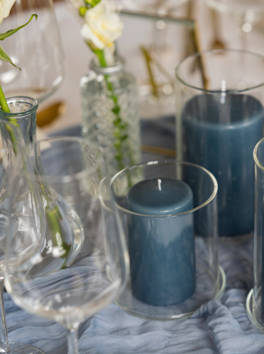 Mehrere Glasbehälter mit blauen Kerzen und Blumen auf einem Tisch.