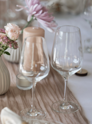 Zwei Weingläser und eine Vase mit Blumen auf einem elegant gedeckten Tisch.