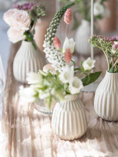 Zarte Blumen in eleganten Vasen auf einem Tischarrangement.